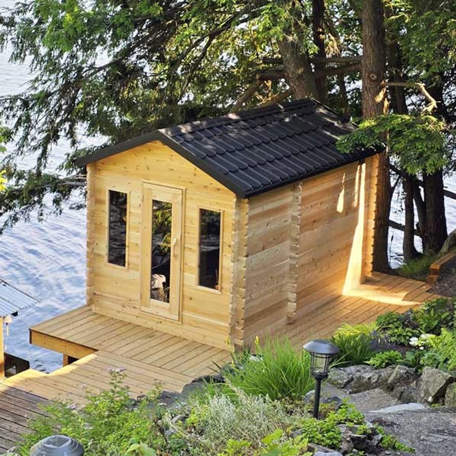 Rustic cedar cabin sauna surrounded by forest, featuring a front porch and chimney