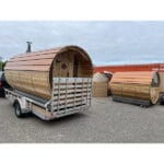 Fully assembled barrel sauna on a trailer with cold tub, log rack, generator, and cedar outdoor shower