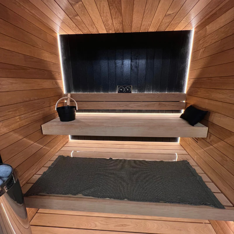 Interior of Auroom Vulcana luxury modern sauna showing golden thermo-aspen, dark Ignite accents, glass front, and two-tier benches