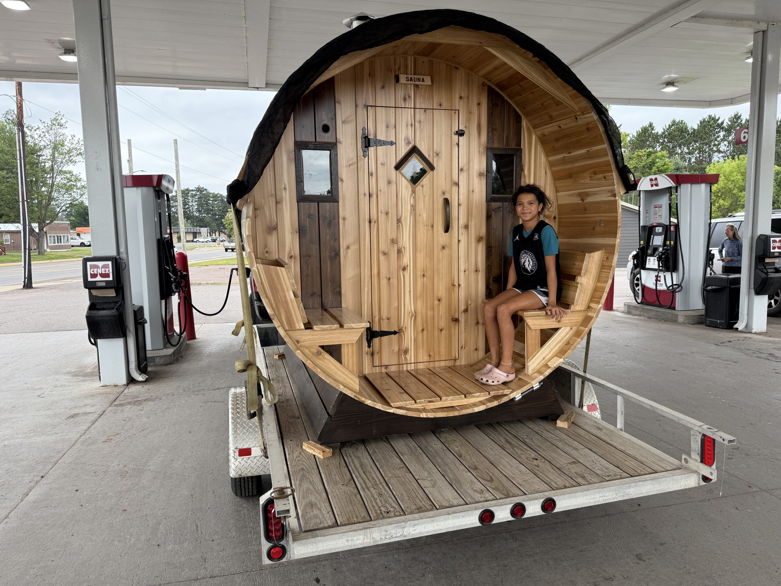 Paizlee sitting on the Cedar Sense barrel sauna during a gas stop on the way to Sturgeon Bay Wisconsin