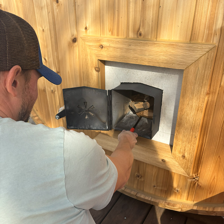 Sasha lighting the wood stove in his BanyaHouse mobile barrel sauna