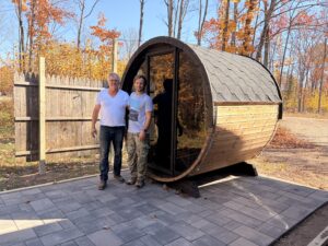 Cody and his father standing outside the completed barrel sauna at his Wisconsin Airbnb